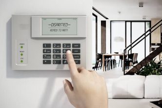 Woman hand above burglar alarm system equipment hanging on the wall.